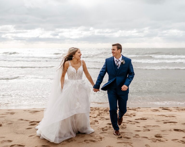 man and wife in wedding dress and suit walking on beach in south haven, mi